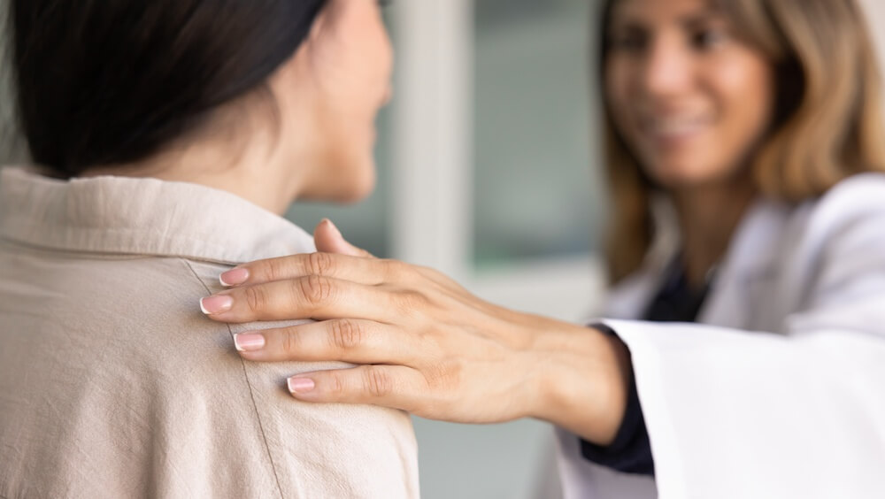 Connection and trust between doctor and patient. Young female therapist put her hand on woman patient shoulder, offers comfort.