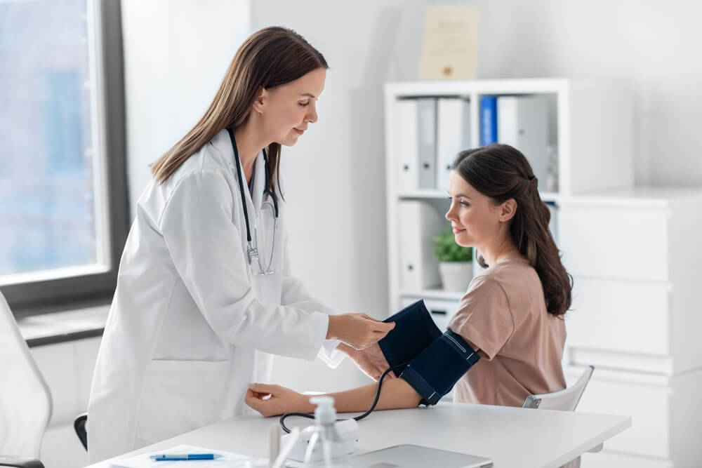 Female doctor with tonometer measuring woman patient's blood pressure at hospital.